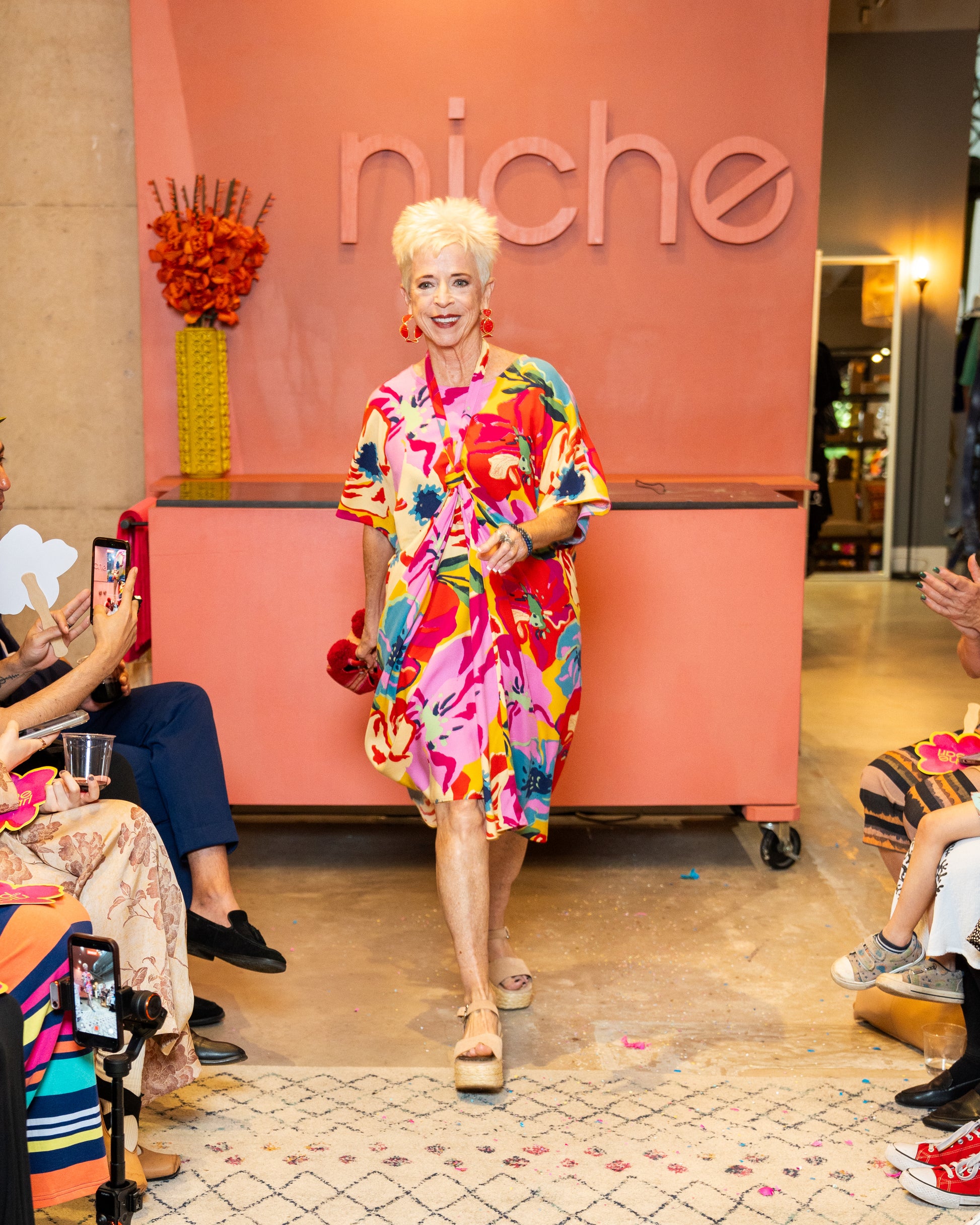 Woman in a colorful dress standing in front of a 'niche' branded wall.