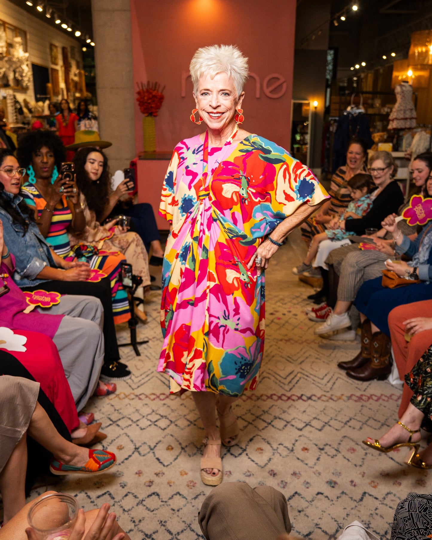 Woman in a colorful dress walking on a runway with an audience in a fashion show setting.