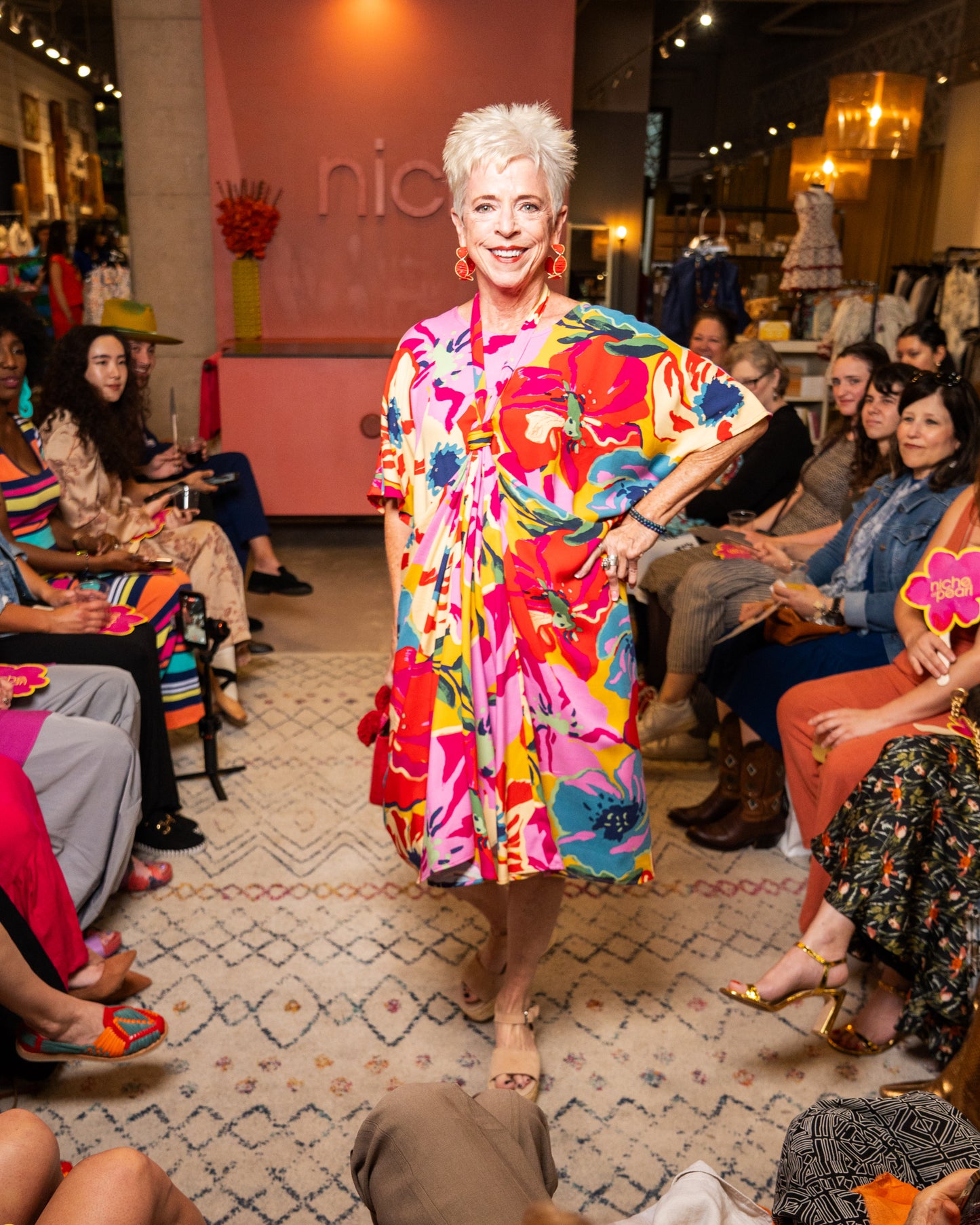 Woman in a colorful dress walking on a runway with an audience in a fashion show setting.