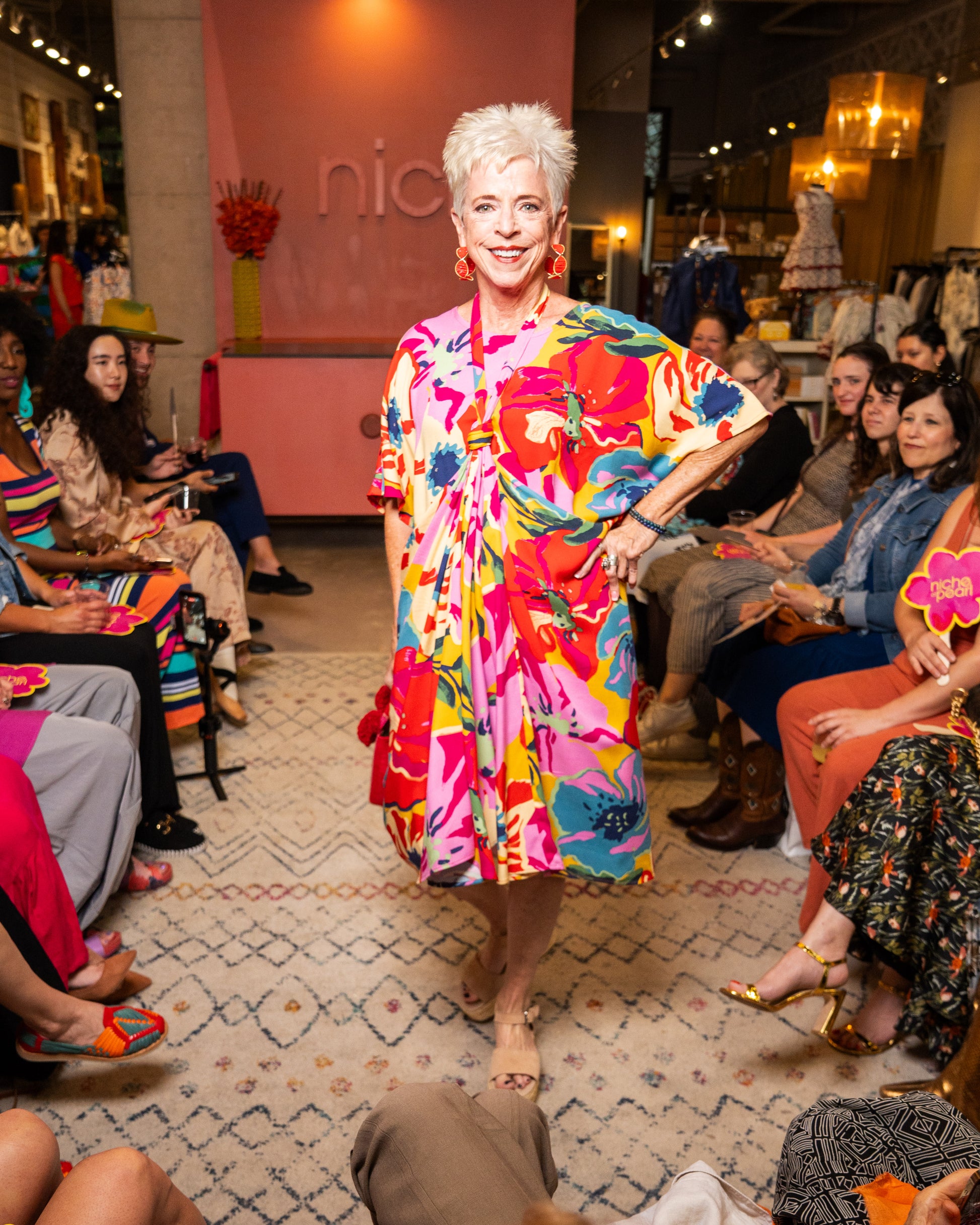Woman in a colorful dress walking on a runway with an audience in a fashion show setting.