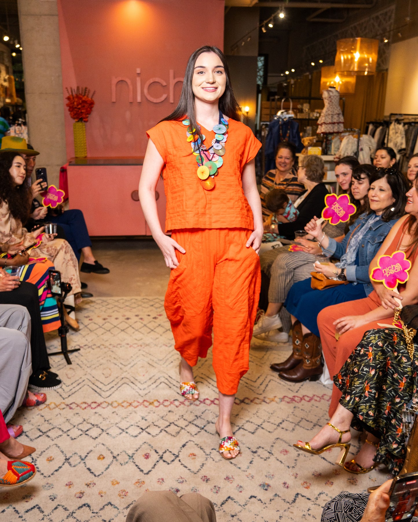 Model wearing an orange set and pant with colorful necklace at a fashion event