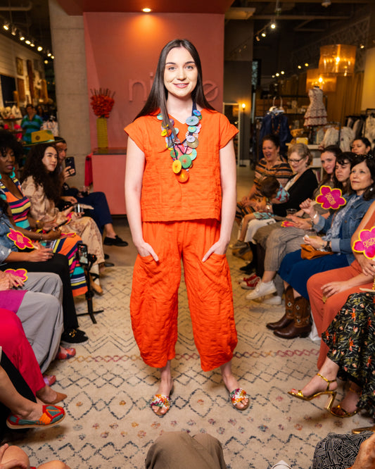Model wearing an orange set and pant with colorful necklace at a fashion event