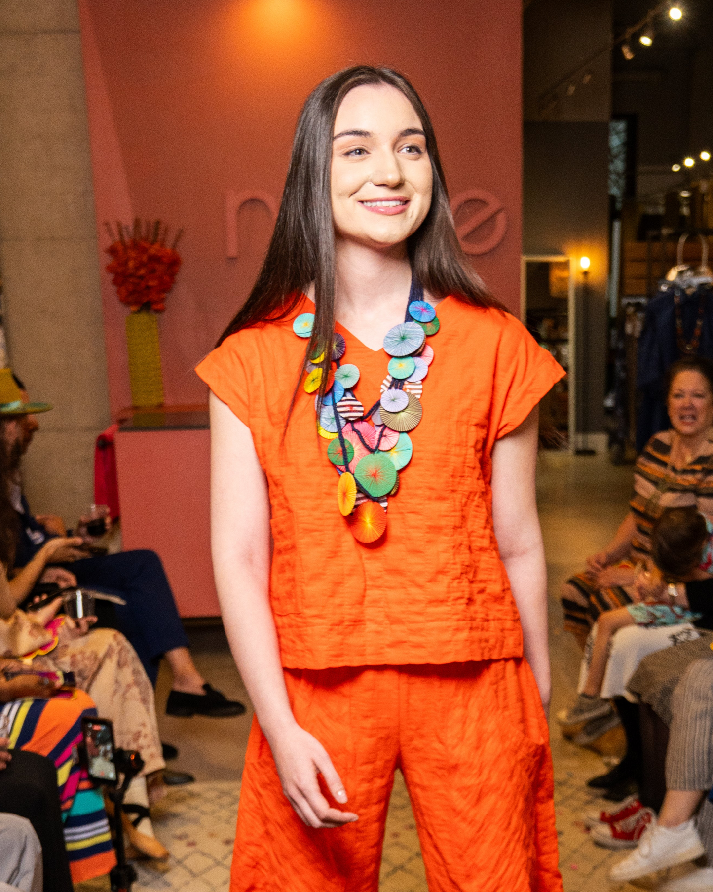 Woman in an orange outfit with a colorful necklace at a fashion event.