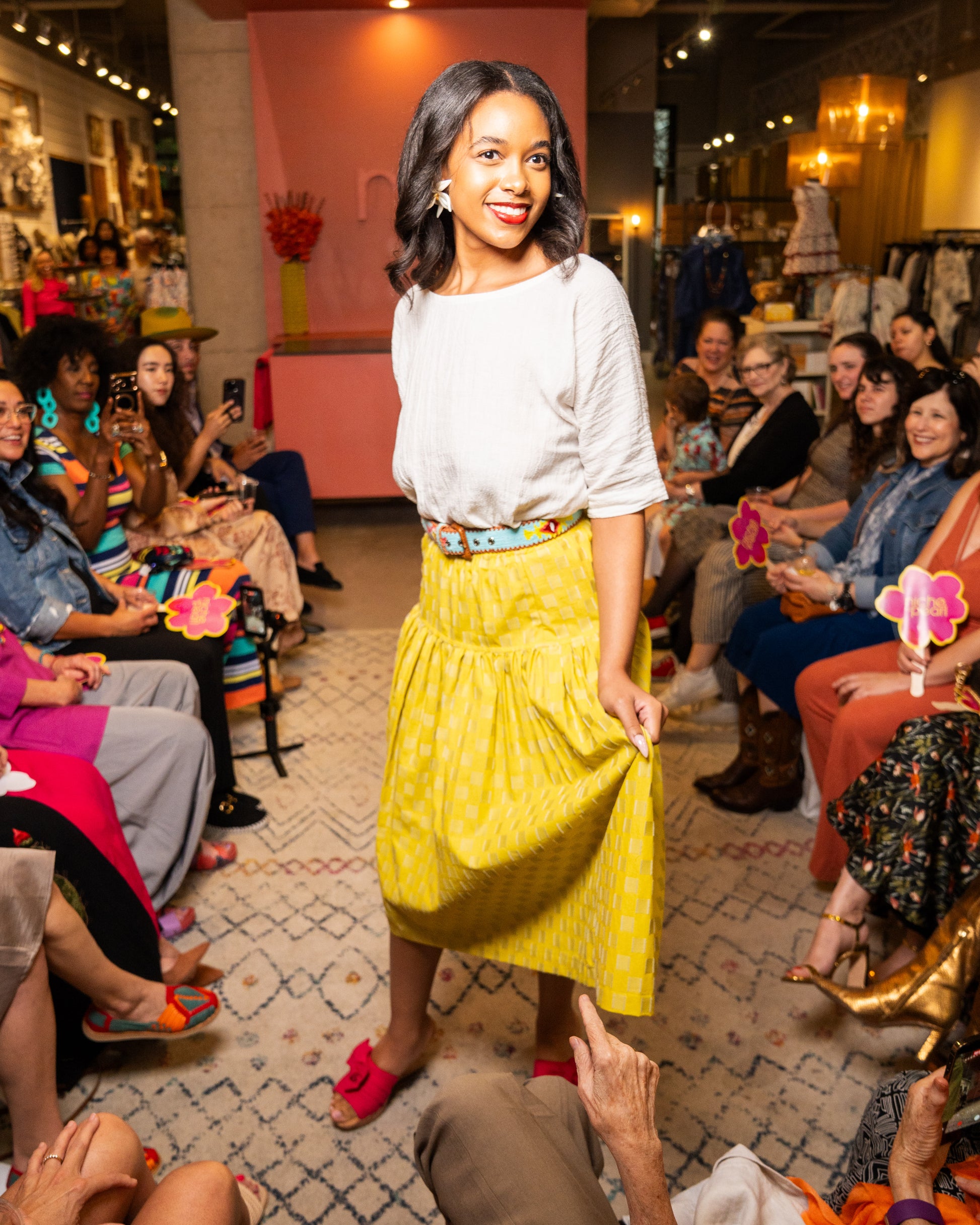 Woman in a yellow skirt and white top standing in front of an audience at a fashion event.