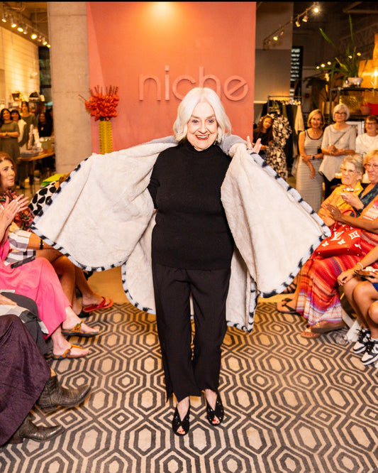 model walking down runway wearing a black top with black and grey faux fur shawl, black pants and black shoes