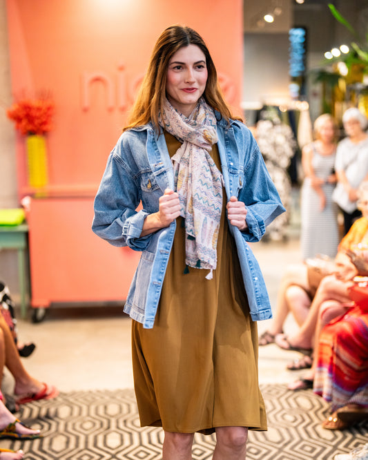 model in a scarf and denim jacket over an ochre knee length dress