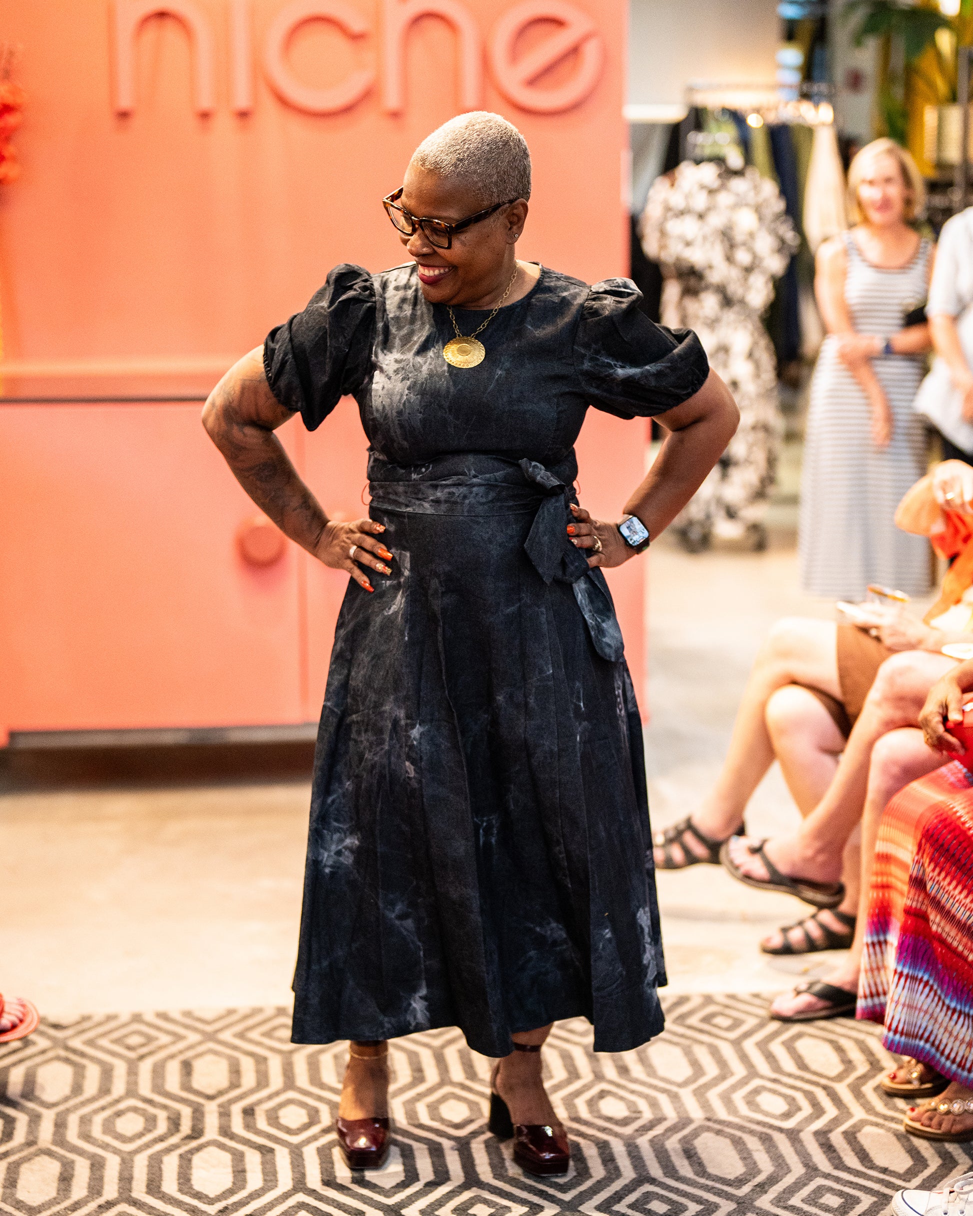 model wearing a twill washed black denim midi dress with round neckline, short puff sleeve, sash tie, full skirt and back zipper closure.