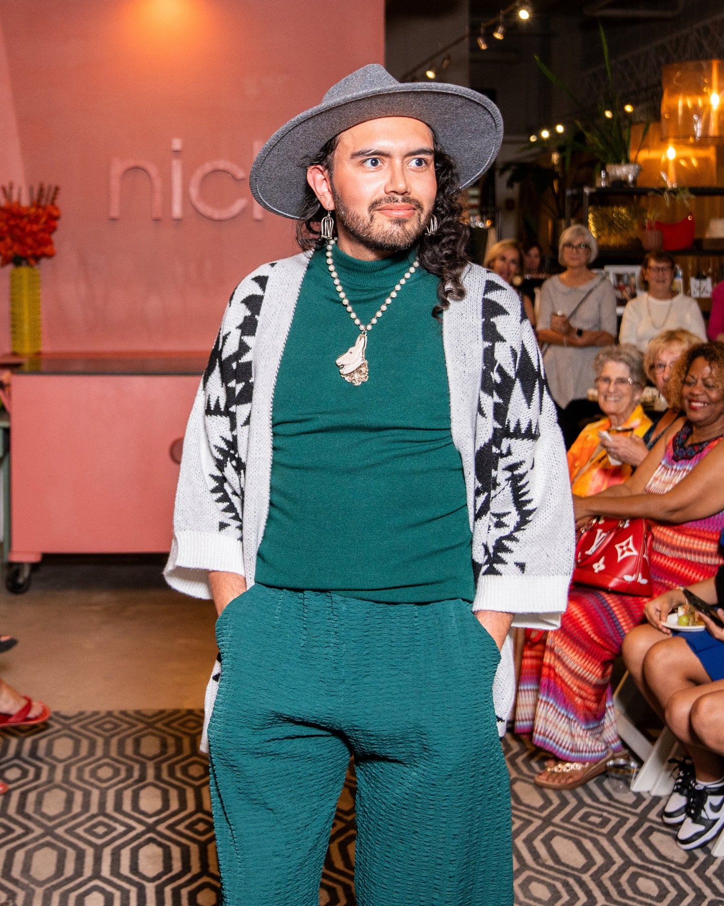 model posing for people wearing an aztec print grey and black cardigan with green pants and grey hat