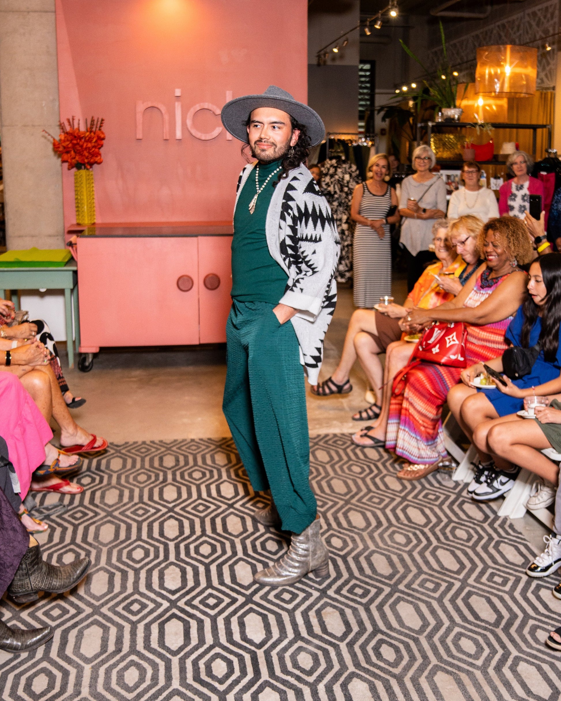 model posing for people wearing an aztec print grey and black cardigan with green pants and grey hat