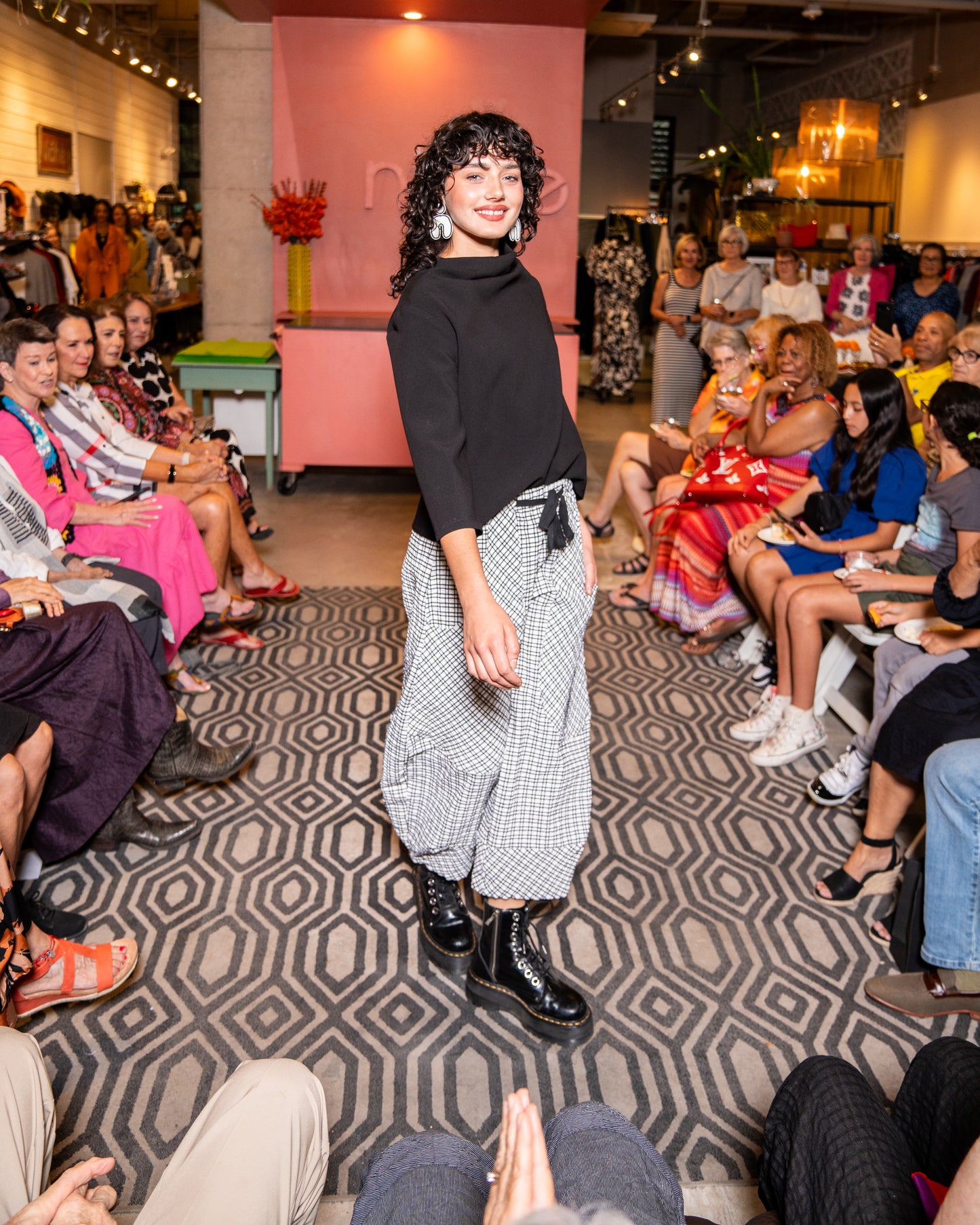 model walking down runway wearing black cowl top with 3/4 sleeves and black and white check pants with black tie belt