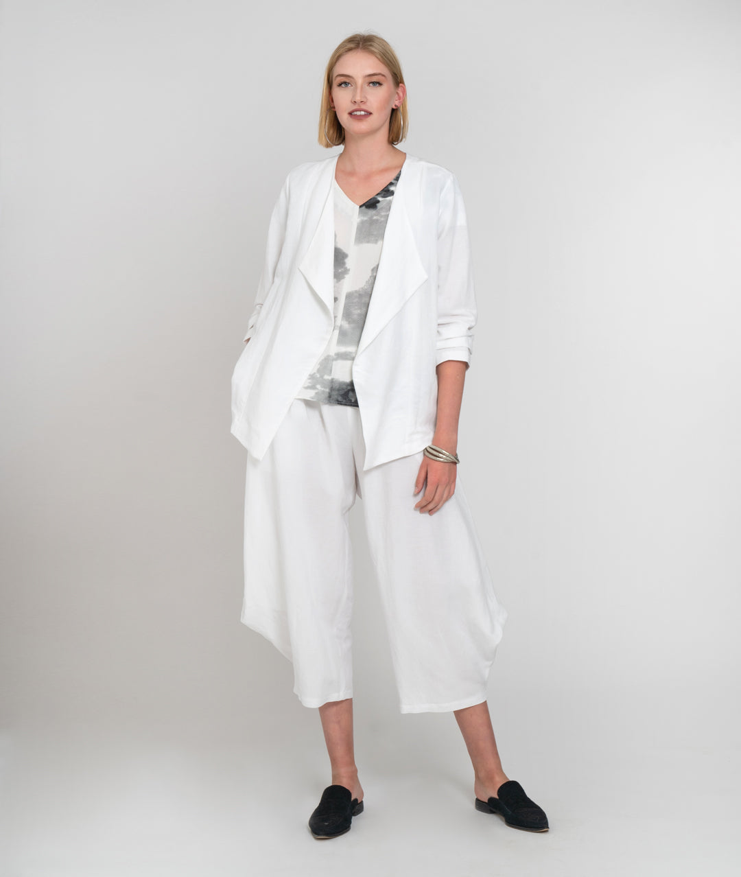 model in a wide white pant with a grey and white print top, and a white jacket with an exaggerated collar