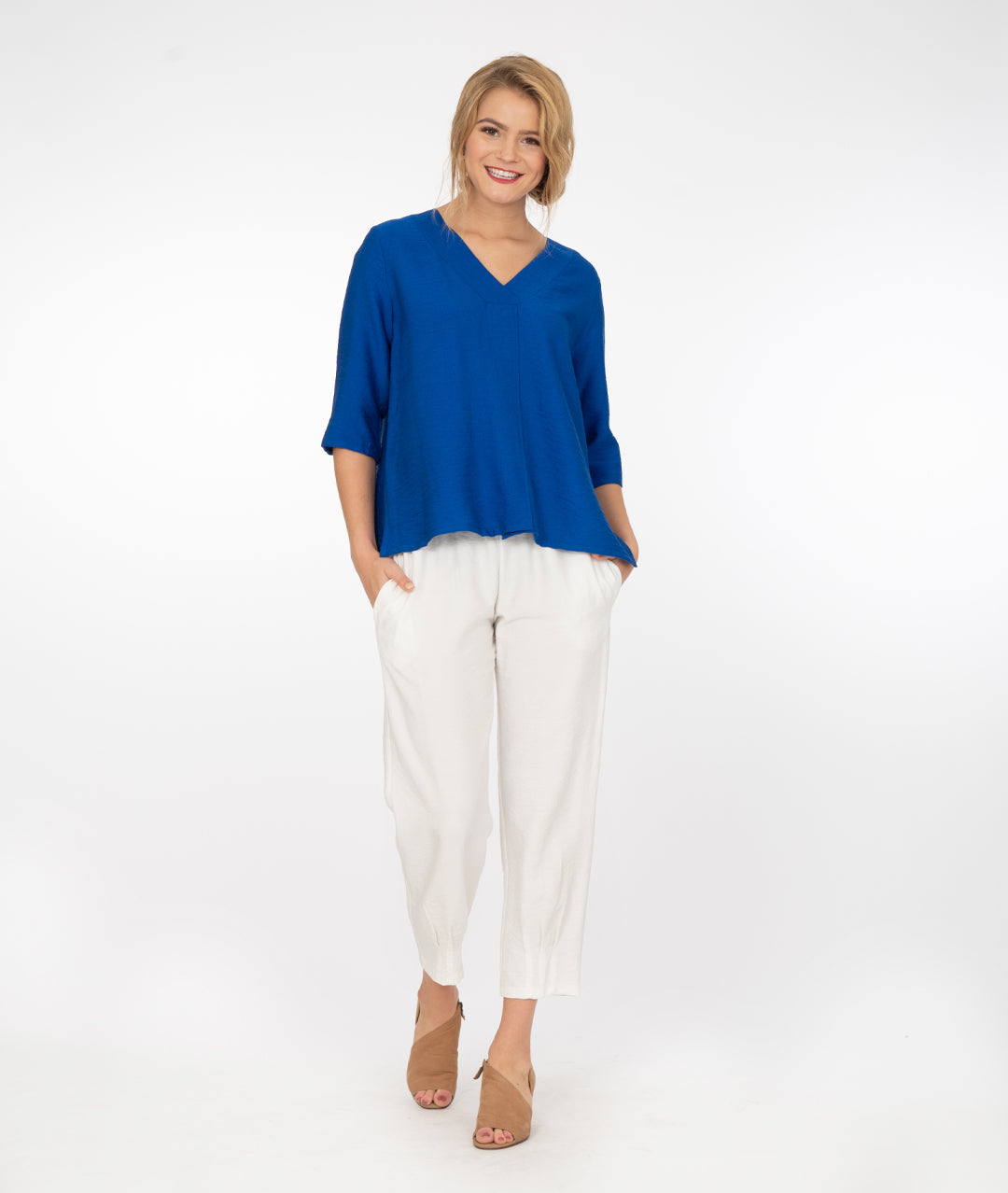 model in a v neck electic blue top with white pants, in front of a white background