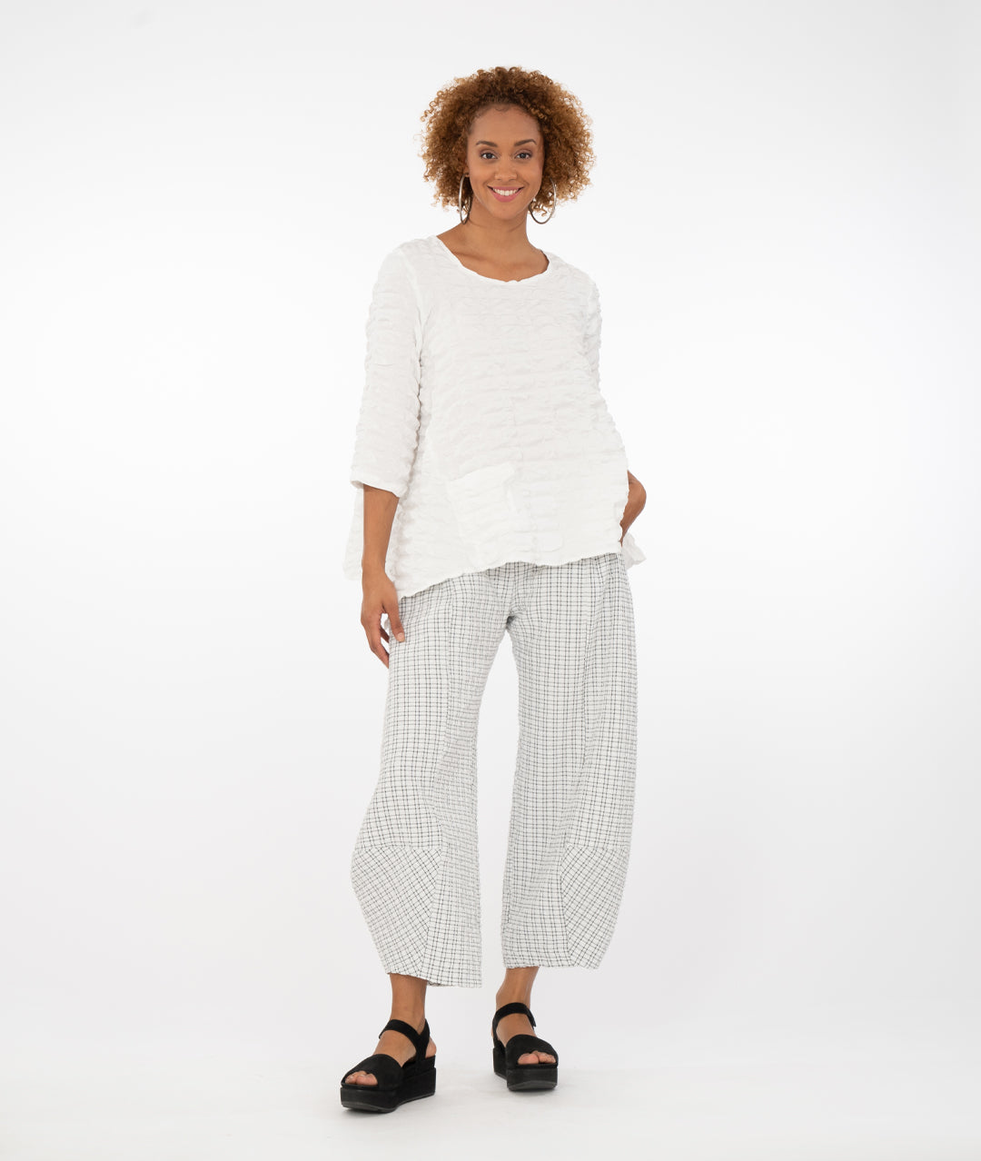 model in a white and black plaid wide leg pant with a tapered ankle, worn with a white pull over top with 3/4 sleeves, dipped hem on either side, and a single square hip pocket