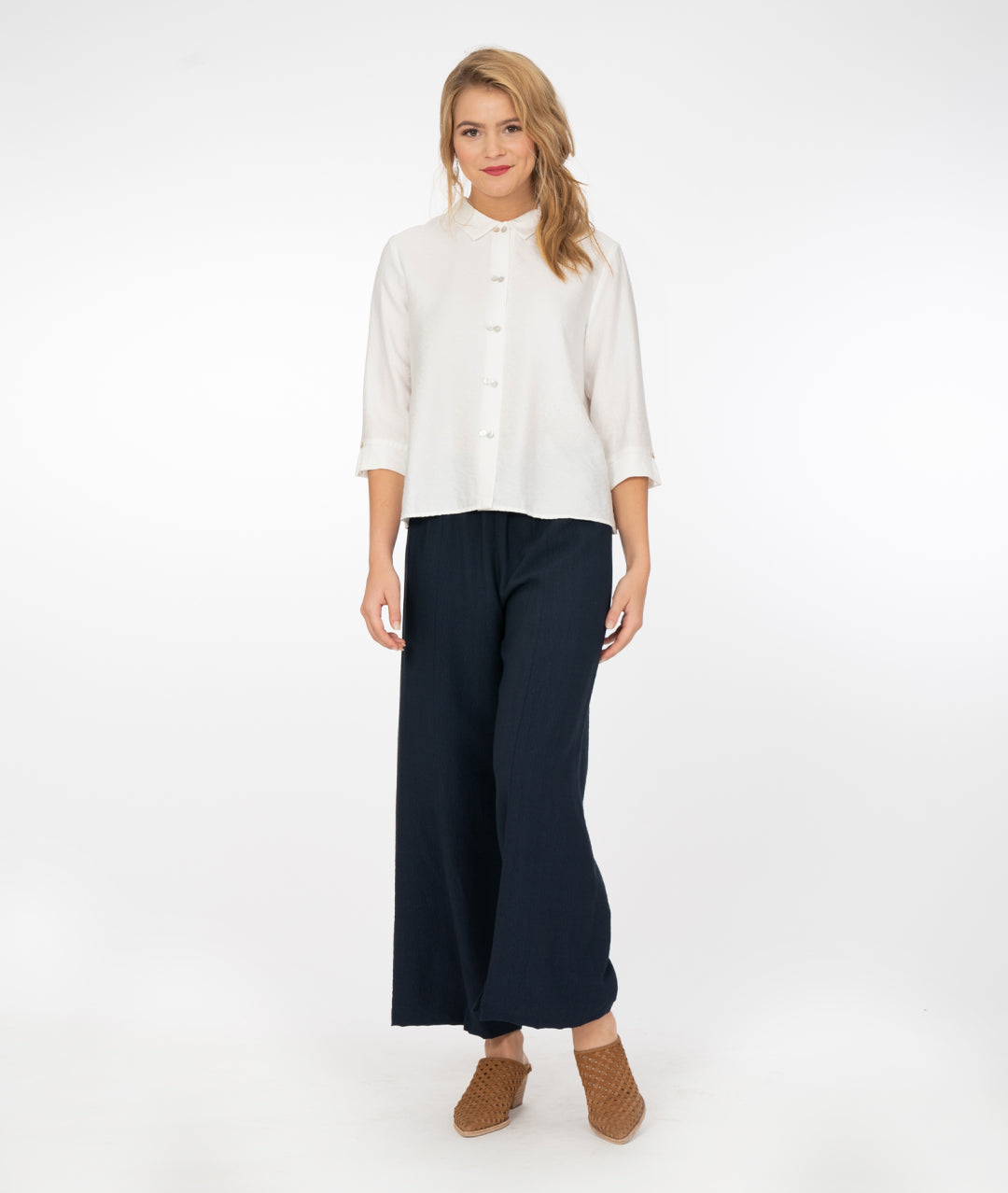 blonde model wearing a white button up shirt with navy blue pants in front of a white background