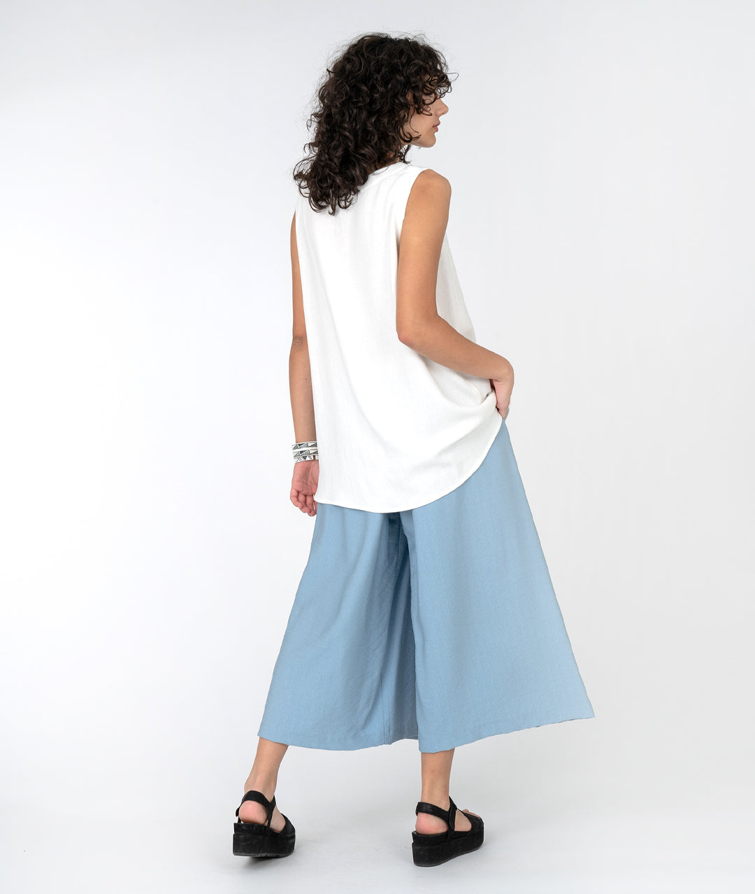 model in a long white tank with a wide leg light blue pant with an overlap panel in the front
