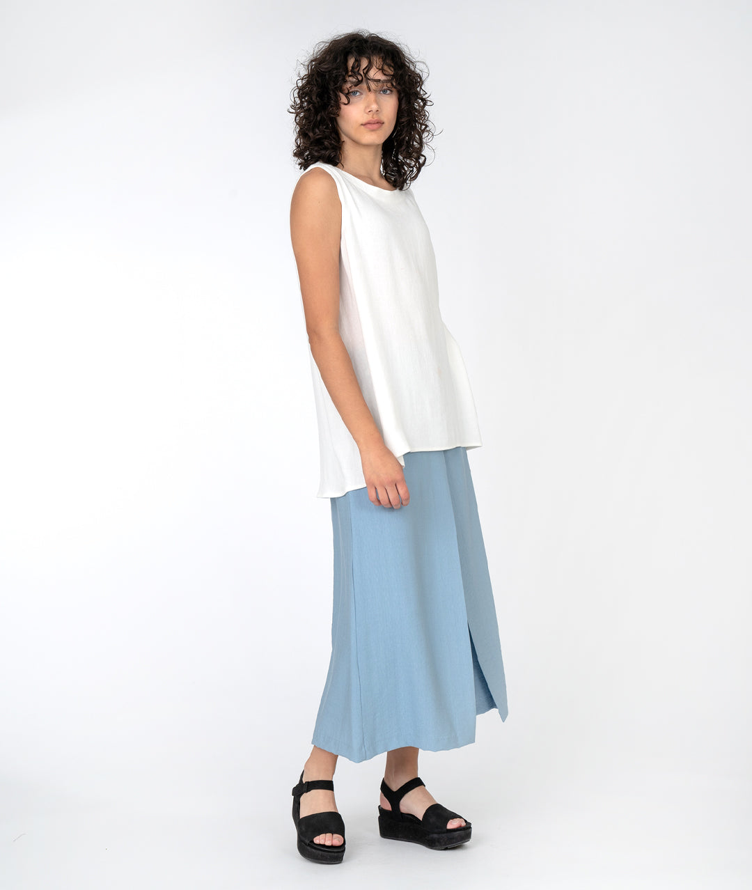 model in a long white tank with a wide leg light blue pant with an overlap panel in the front