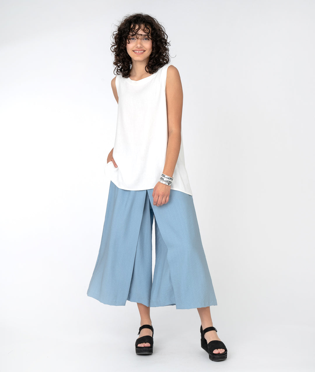 model in a long white tank top with a wide leg light blue pant with an overlapping panel in the front from each leg