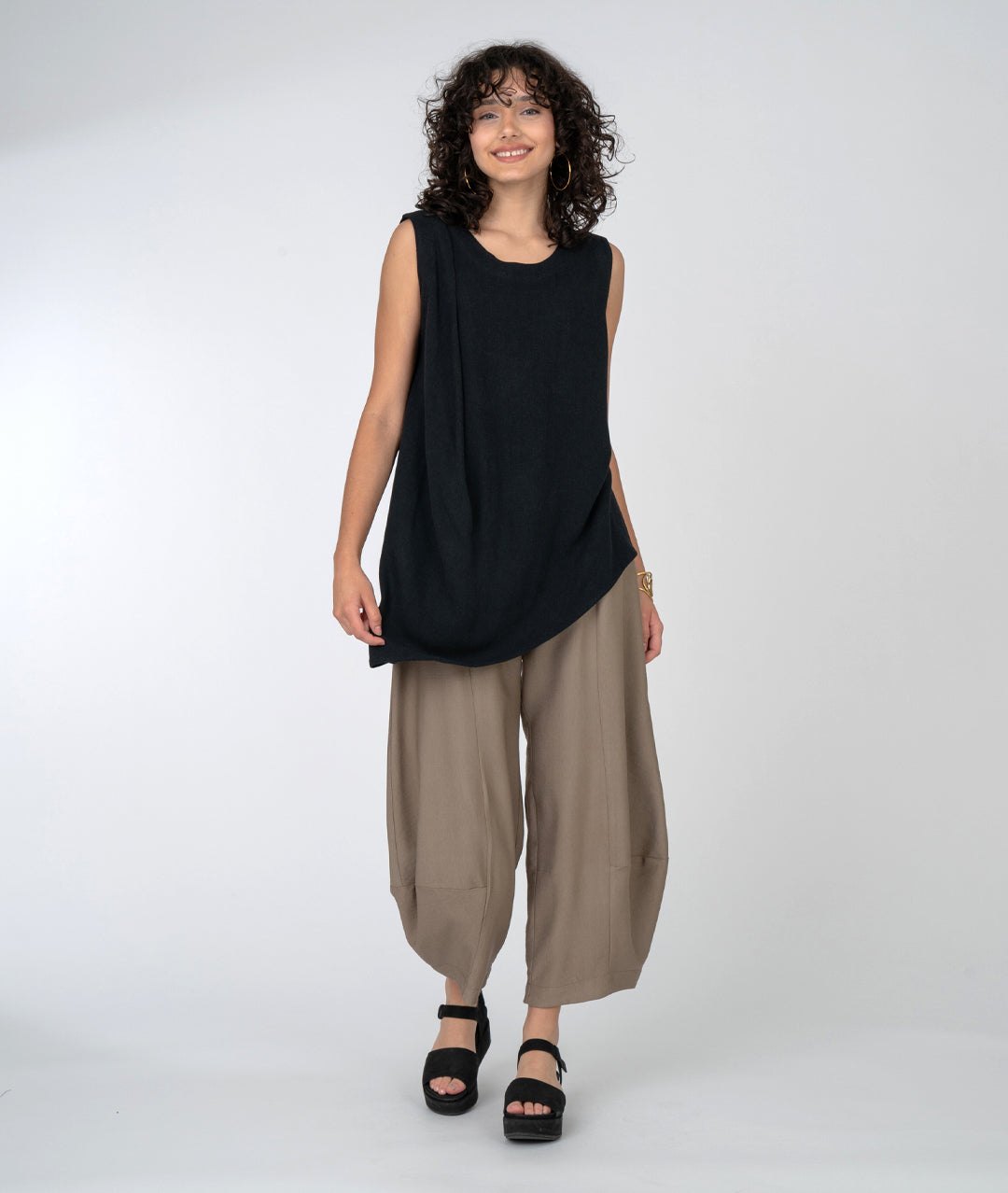 Sleeveless top with beautiful gather at one shoulder and asymmetrical hemline. Taupe pants and black platform sandals.