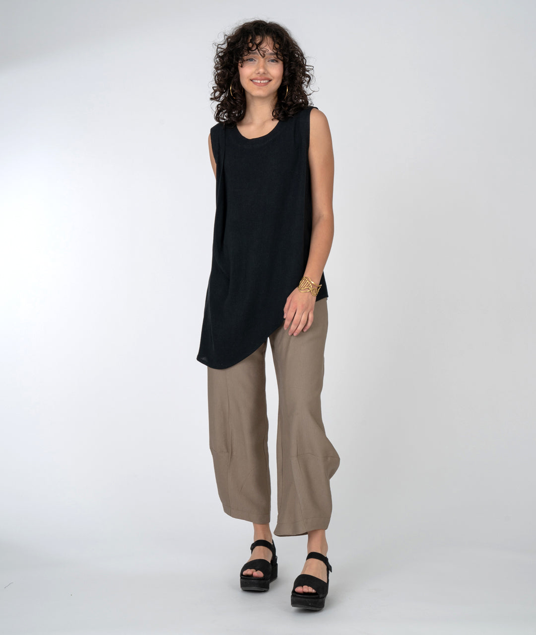 Sleeveless top with beautiful gather at one shoulder and asymmetrical hemline. Taupe pants and black platform sandals.