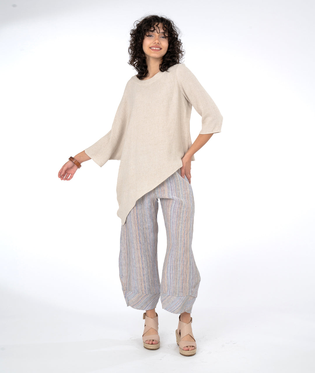 model in a wide leg multi color stripe pant with an oatmeal color cocoon style top with on batwing sleeve and an asymmetrical draped hem