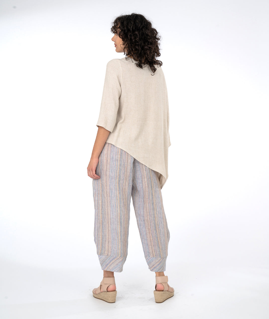 model in a wide leg multi color stripe pant with an oatmeal color cocoon style top with on batwing sleeve and an asymmetrical draped hem