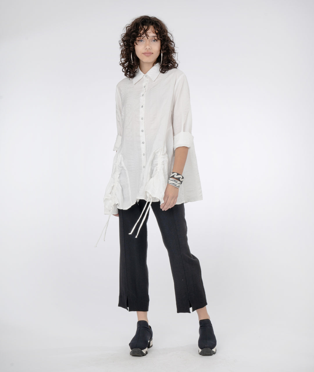 model in a black pant with a long white button down blouse with rolled up sleeves and a gather detail at either hip