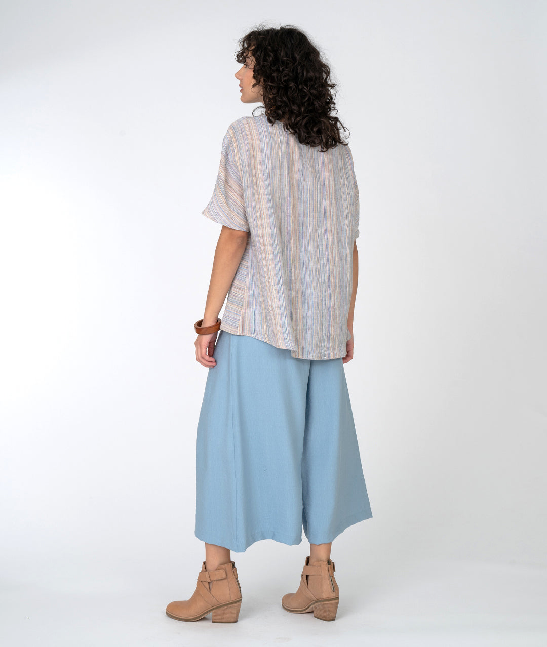 model in a wide leg blue pant with a multicolor stiped top with an asymmetrical panel