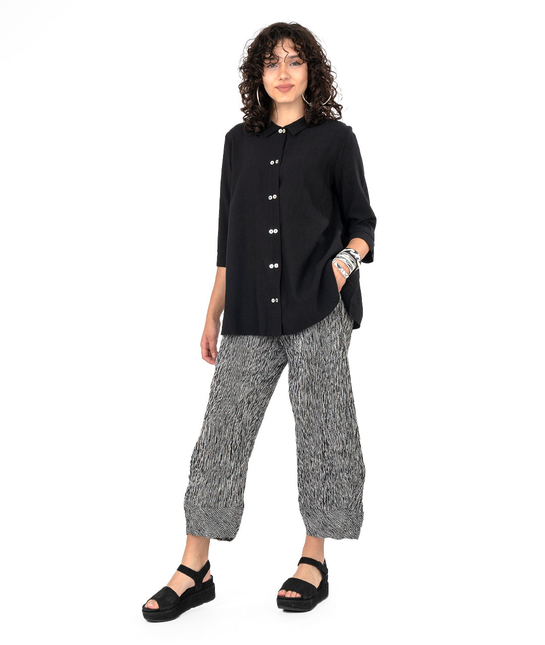 model in a black and white striped pant with a tapered ankle. worn with a long black button down blouse with a 3/4 sleeve and a twin button detail.