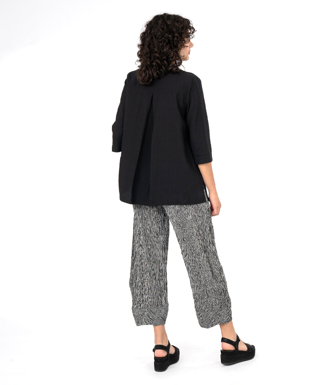 model in a black and white striped pant with a tapered ankle. worn with a long black button down blouse with a 3/4 sleeve and a twin button detail.