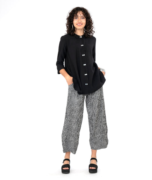 model in a black and white striped pant with a tapered ankle. worn with a long black button down blouse with a 3/4 sleeve and a twin button detail.