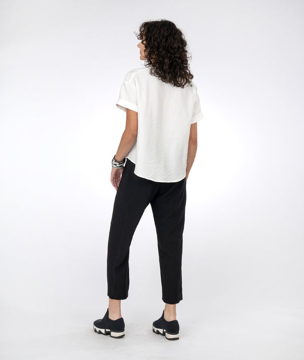 model in a slim black pant with a vneck white top with short sleeves and a twin button detail down the front center