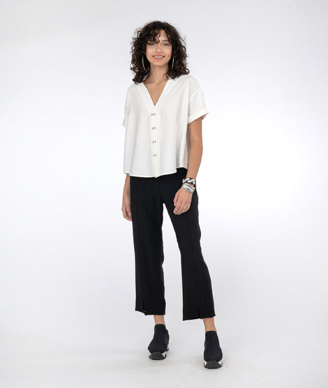 model in a slim black pant with a vneck white top with short sleeves and a twin button detail down the front center