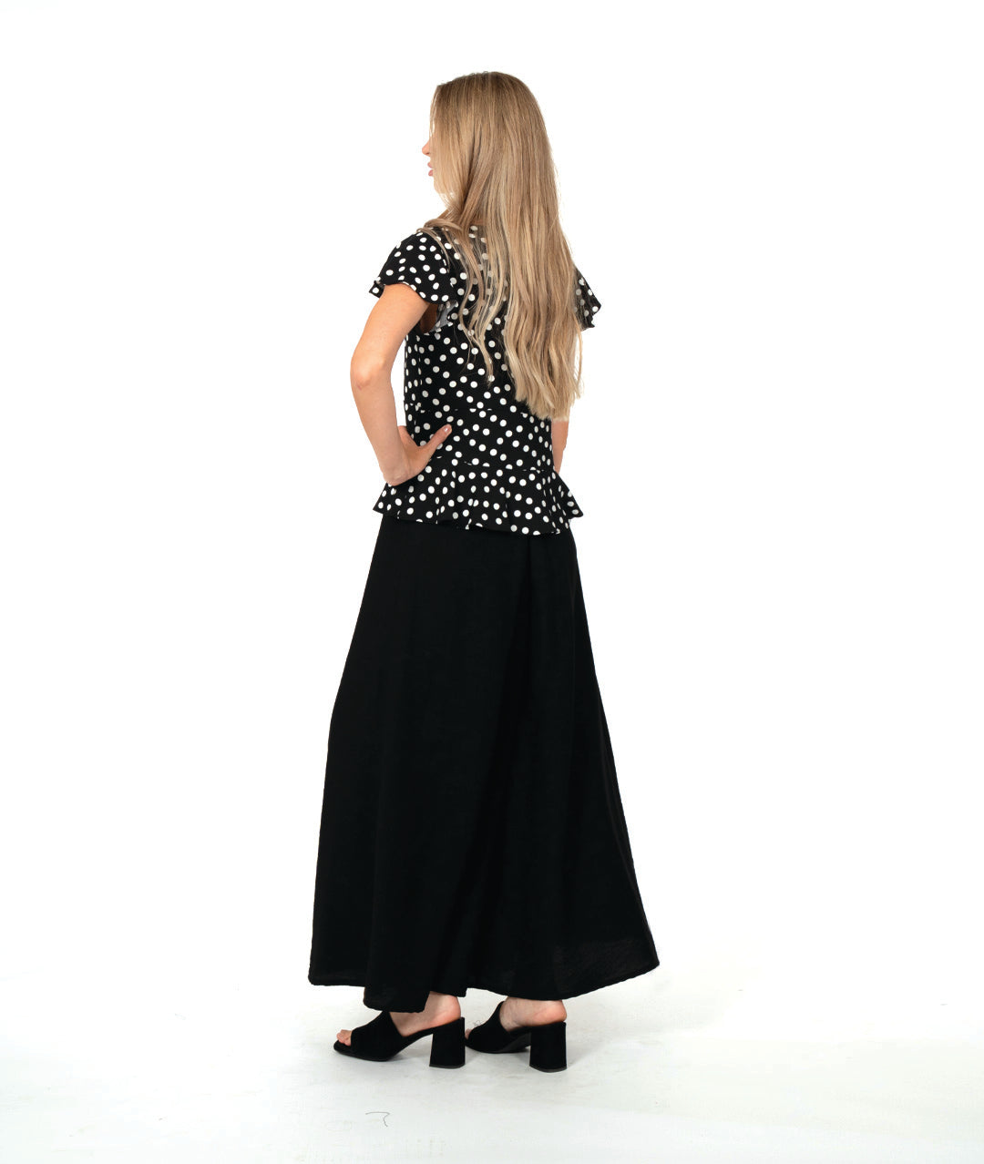 model in a black top with white dots, worn with an ultra wide leg black pant. top is fitted with a v-neck, flutter sleeves and a peplum at the waist