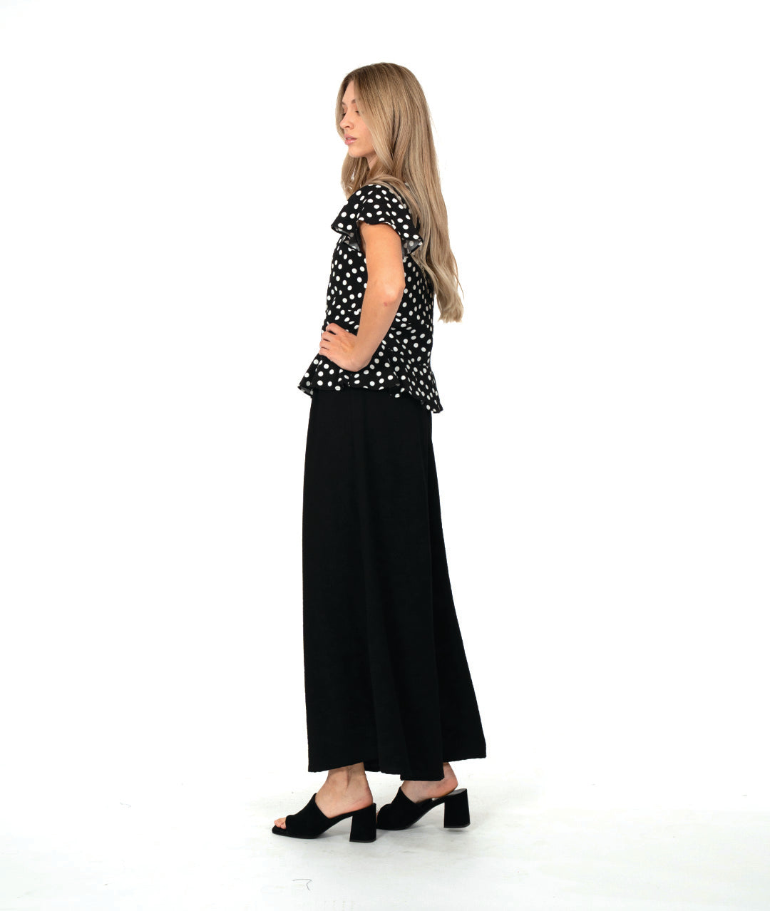 model in a black top with white dots, worn with an ultra wide leg black pant. top is fitted with a v-neck, flutter sleeves and a peplum at the waist