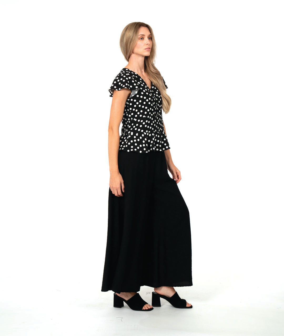 model in a black top with white dots, worn with an ultra wide leg black pant. top is fitted with a v-neck, flutter sleeves and a peplum at the waist