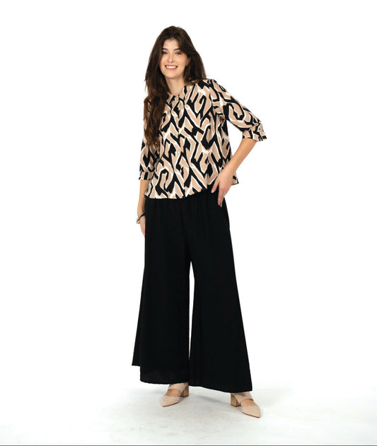 model in a tan, black and white geometric print button down blouse, worn with an ultra wide leg black pant