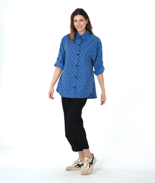 Woman wearing a blue and black checker board patterned blouse and black wide leg pants on a white background