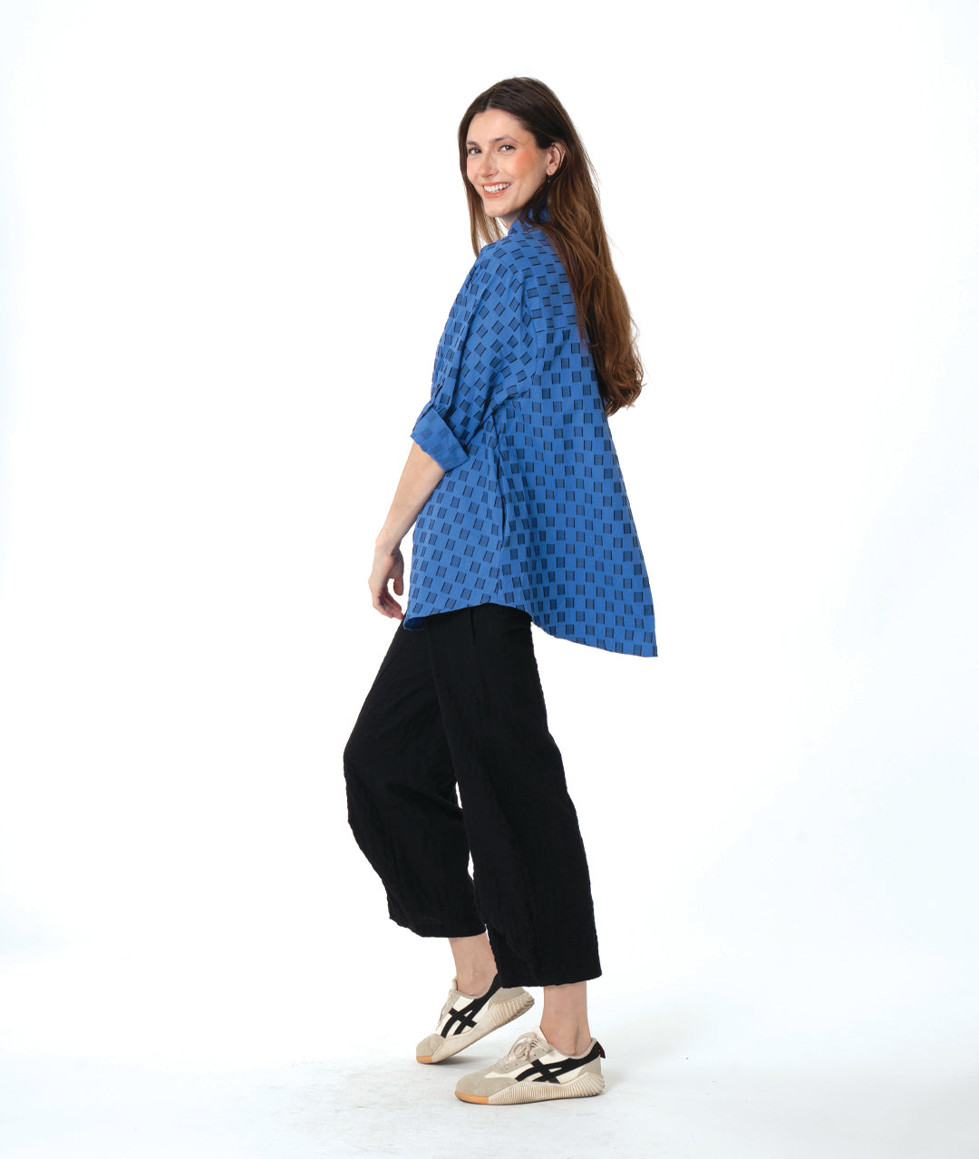 Woman wearing a blue and black checker board patterned blouse and black wide leg pants on a white background