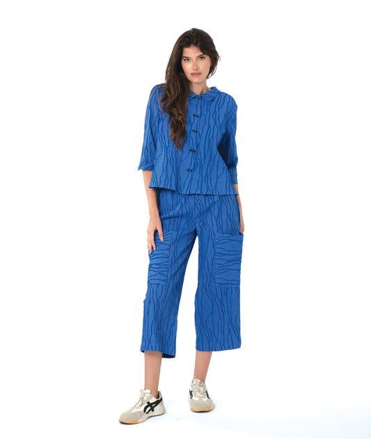 Woman wearing a blue textured pant and matching button down blouse on a white background