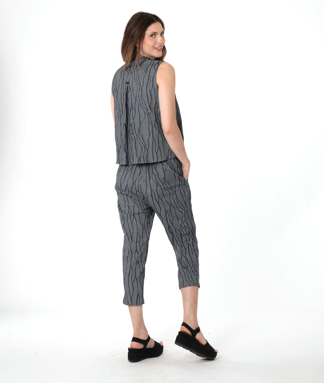 A woman modeling a matching sleeveless top and cropped pants set in a dark gray and black wavy pattern, paired with black platform sandals, against a plain white studio background.