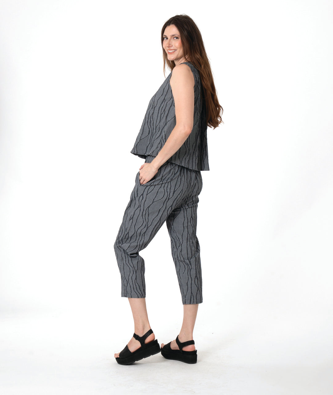 A woman modeling a matching sleeveless top and cropped pants set in a dark gray and black wavy pattern, paired with black platform sandals, against a plain white studio background.