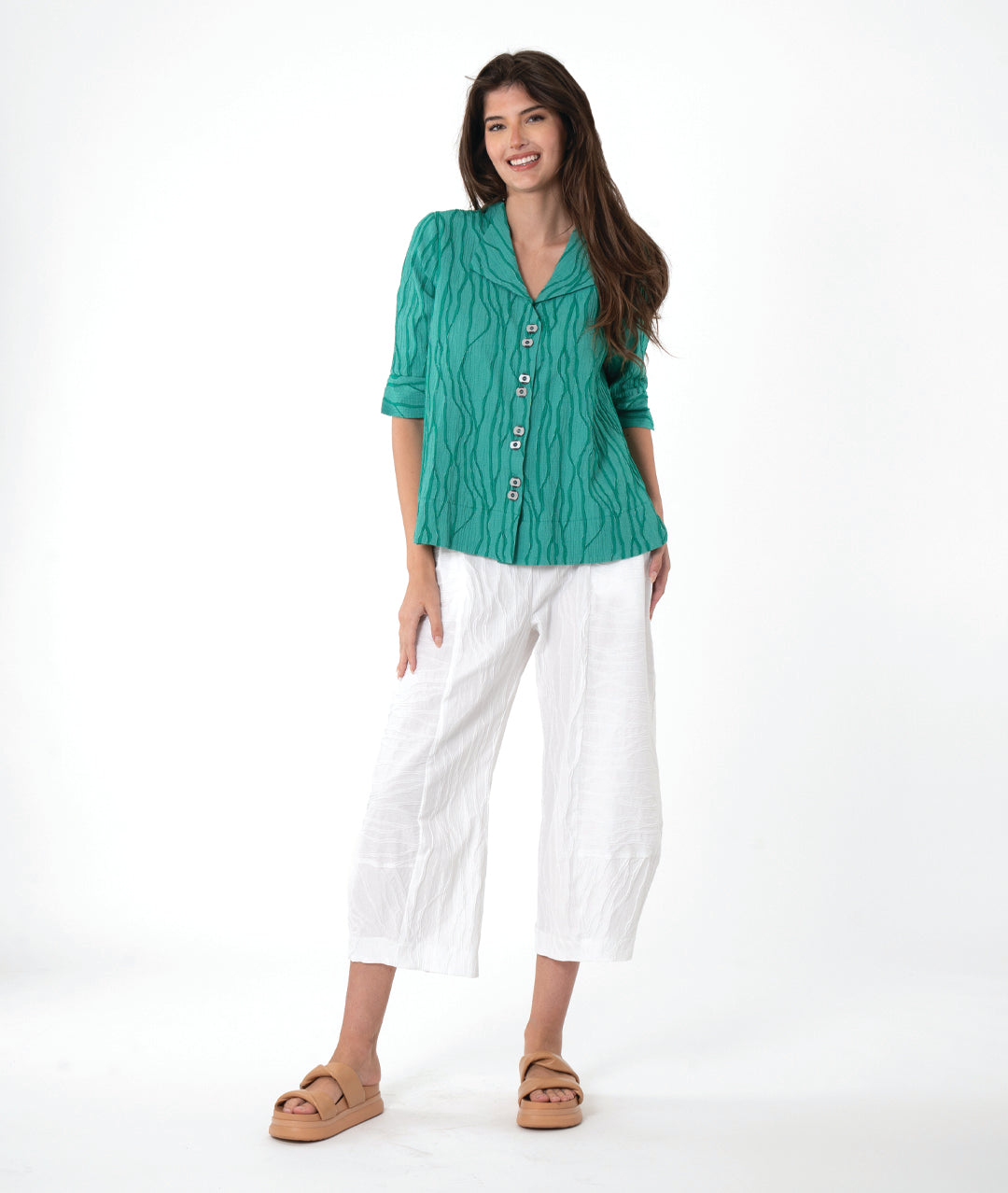 model in a boxy teal textured button down blouse with a flat collar, 3/4 sleeves and a wide hem. worn with a matching white pant
