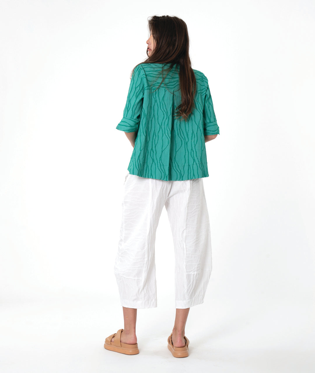 model in a boxy teal textured button down blouse with a flat collar, 3/4 sleeves and a wide hem. worn with a matching white pant