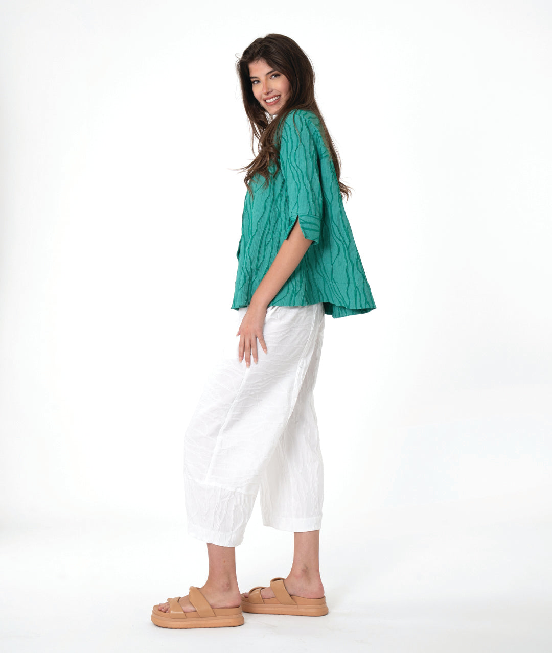 model in a boxy teal textured button down blouse with a flat collar, 3/4 sleeves and a wide hem. worn with a matching white pant