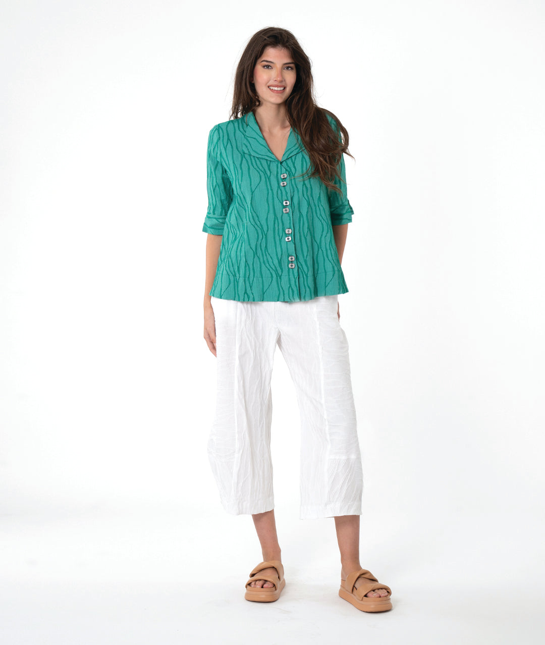 model in a boxy teal textured button down blouse with a flat collar, 3/4 sleeves and a wide hem. worn with a matching white pant