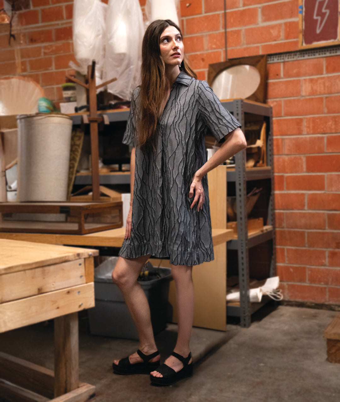 A woman modeling a dark gray wavy pattern pullover a line dress with an open collar, short sleeves and a knee length hem