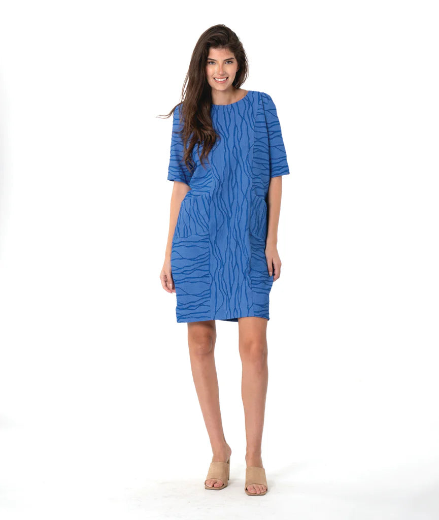 Model wearing pattered violet dress with front pockets on white background.