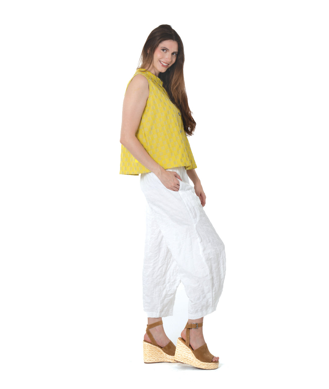 model in a yellow two toned sleeveless blouse, with a textured white pant with tucks below the knee 