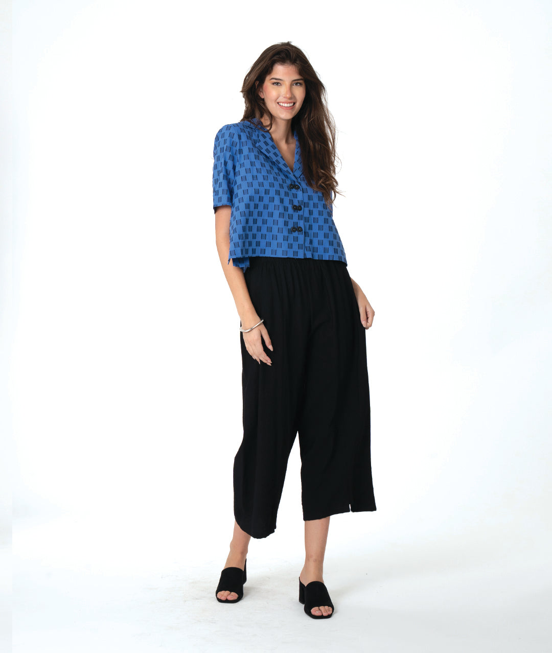 Woman wearing a blue and black checker board patterned top and black wide leg pants on a white background