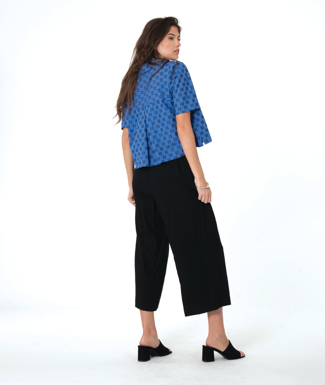 Woman wearing a blue and black checker board patterned top and black wide leg pants on a white background